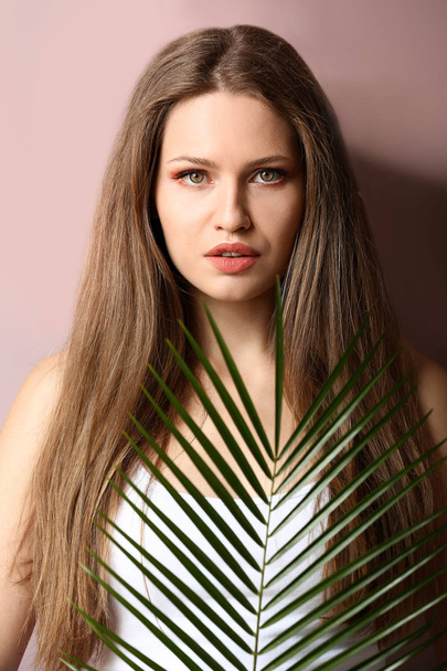 Portrait of beautiful woman with green tropical leaf on color background - Фото, зображення