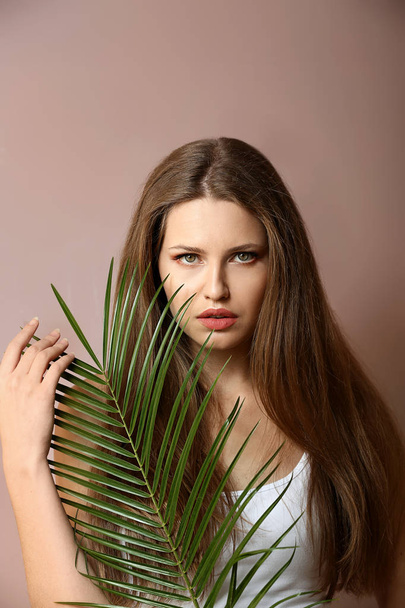 Portrait of beautiful woman with green tropical leaf on color background - Foto, immagini