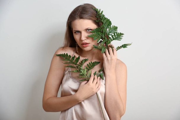 Portrait of beautiful woman with green fern leaves on light background - 写真・画像