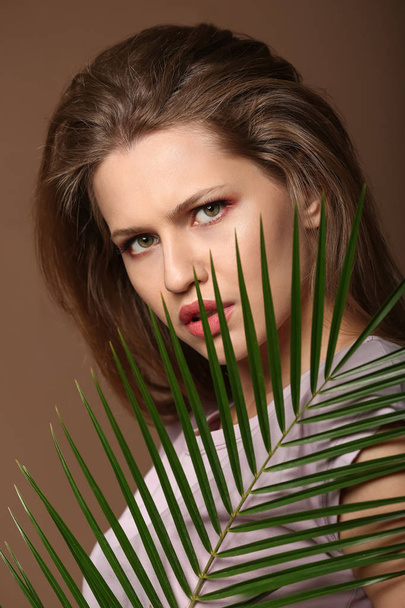 Portrait of beautiful woman with green tropical leaf on color background - Zdjęcie, obraz