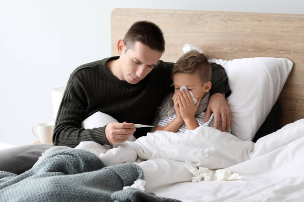 Padre cuidando a su hijo enfermo de gripe en casa
 - Foto, Imagen