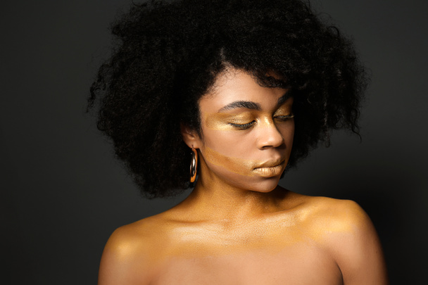Mujer afroamericana con pintura dorada en su cuerpo sobre fondo negro
 - Foto, imagen