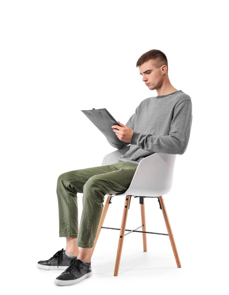Jonge man met Klembord zitten in fauteuil op witte achtergrond - Foto, afbeelding