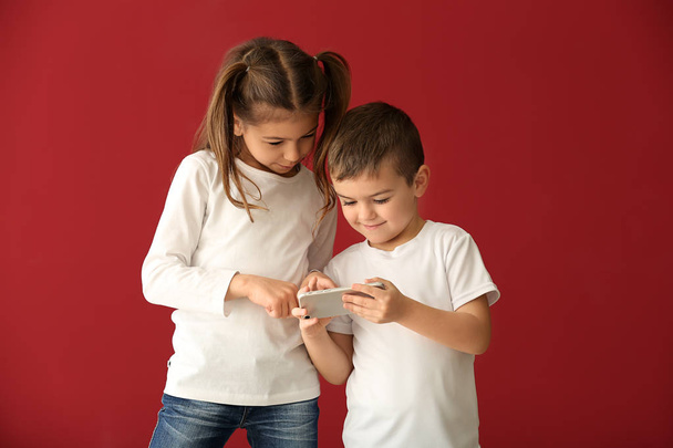 Schattige kleine kinderen spelen met smartphone op kleur achtergrond - Foto, afbeelding