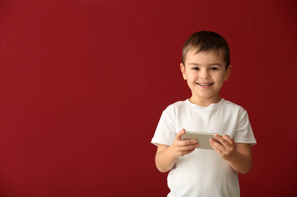 Schattige kleine jongen spelen met smartphone op kleur achtergrond - Foto, afbeelding