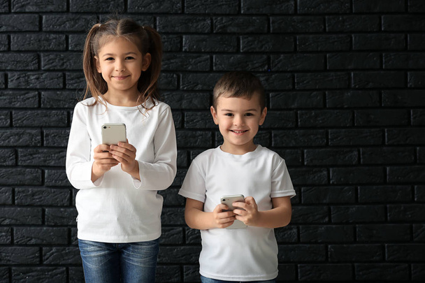 Aranyos kis gyerekek játszó okostelefonok sötét háttér - Fotó, kép