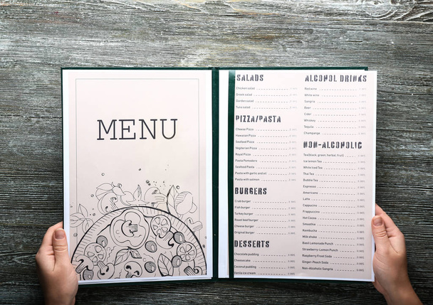 Female hands with menu on wooden table - Foto, imagen