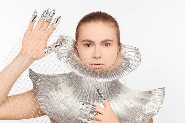 Futuristic woman dressed in iron clothes and with fingers rolled up in foil. White background - Foto, Imagen