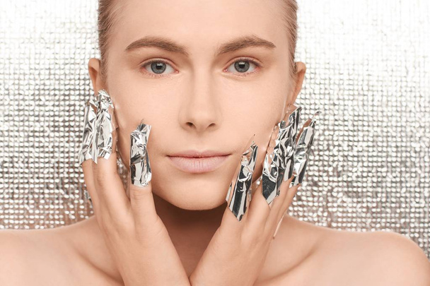 Portrait of a young beautiful woman on a futuristic background, with fingers wrapped in foil - Φωτογραφία, εικόνα