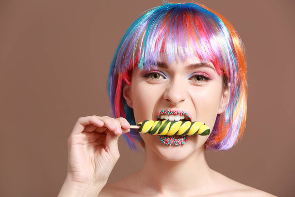 Beautiful young woman with unusual makeup and sweet lollipop on color background - Zdjęcie, obraz