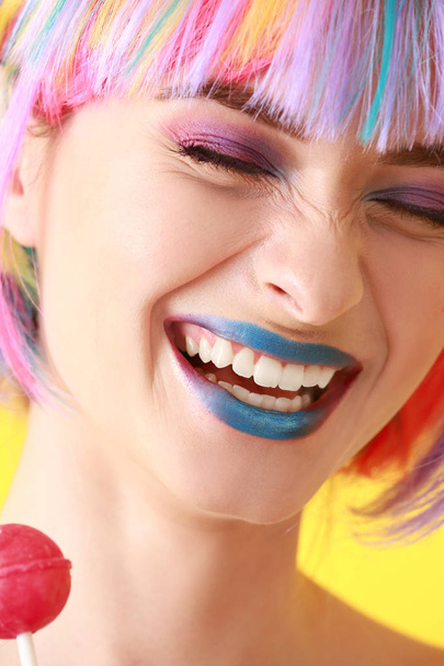 Laughing young woman with unusual makeup and sweet lollipop on color background, closeup - Фото, зображення