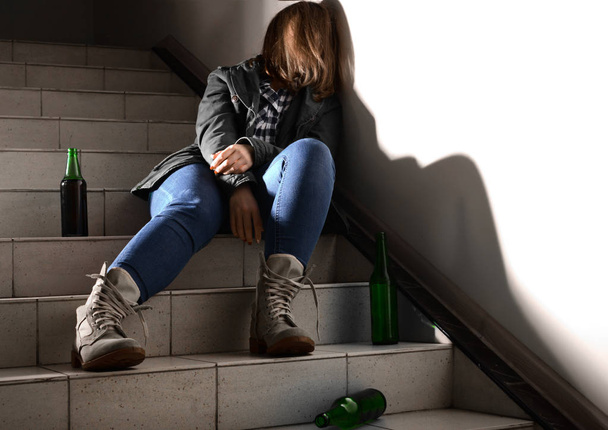 Unconscious young woman with empty bottles sitting on stairs. Concept of alcoholism - Photo, Image