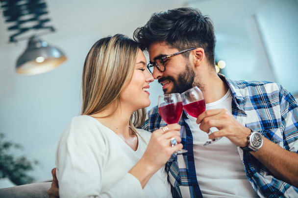 Молода пара насолоджується вином вдома. Вони сидять поруч і п'ють червоне вино
. - Фото, зображення