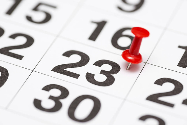 PIN op de datum nummer 23. De 23e dag van de maand is gemarkeerd met een rode punaise. PIN op de kalender - Foto, afbeelding