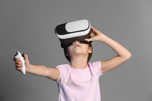 Cute girl with virtual reality glasses on grey background - Fotoğraf, Görsel