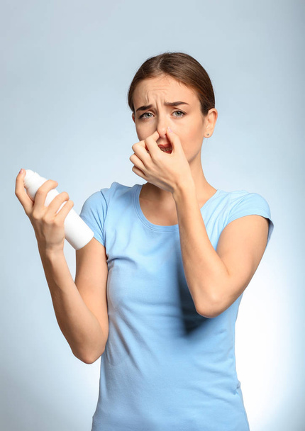 Красивая молодая женщина с дезодорантом, чувствующая запах пота на светлом фоне. Концепция использования дезодоранта
 - Фото, изображение