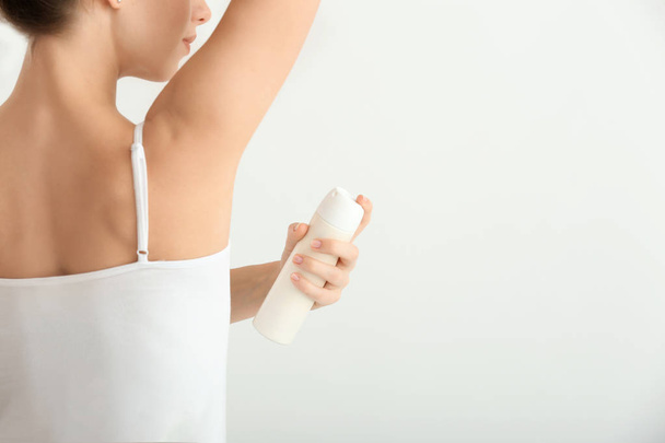 Mooie jonge vrouw met deodorant op lichte achtergrond - Foto, afbeelding