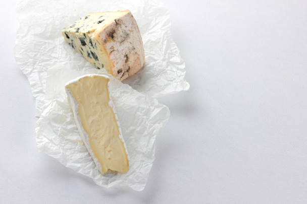 Camembert and blue cheese on parchment paper. Pieces of various cheese on white background. Dorblu and soft cheese in the style of minimalism. Eco-friendly dairy products - Photo, image