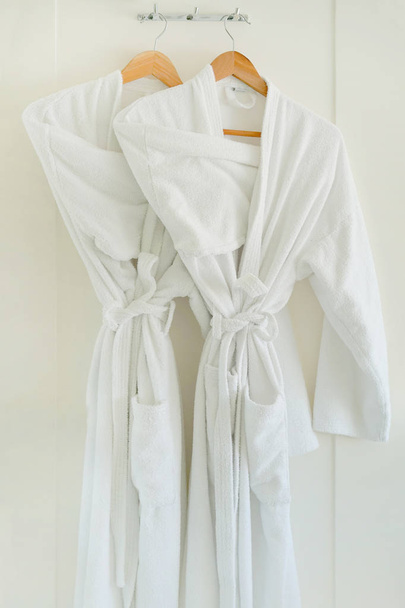 Two white coats hanging on the door. Hotel dressing gowns on the door hanger. - Photo, Image