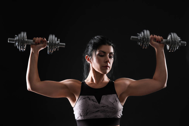 Donna muscolosa sportiva con manubri su sfondo scuro
 - Foto, immagini