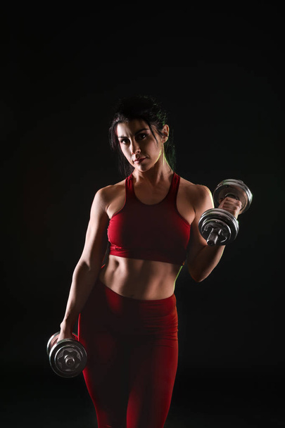 Sporty muscular woman with dumbbells on dark background - Fotó, kép