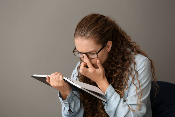 Młoda kobieta z zły wzrok czytanie książki na szarym tle - Zdjęcie, obraz