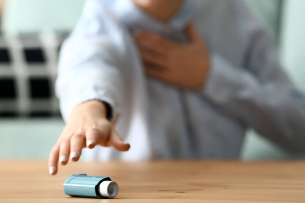 Молодая женщина с приступом астмы берет ингалятор со стола, крупным планом
 - Фото, изображение