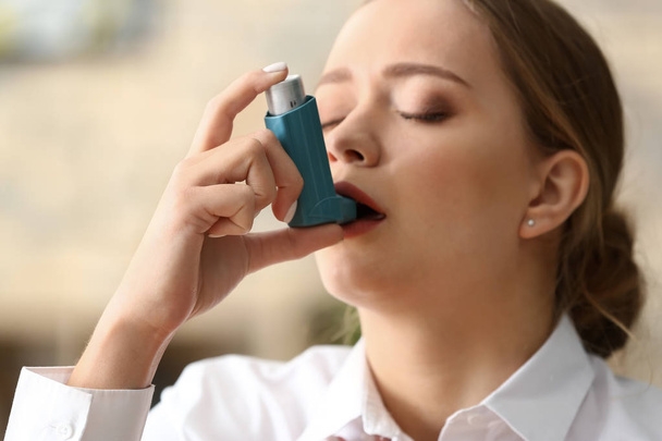 Jonge vrouw met inhalator met astma aanval in kantoor - Foto, afbeelding