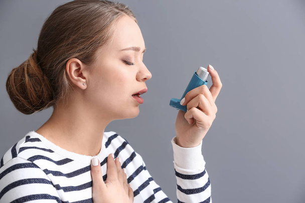Mujer joven con inhalador con ataque de asma sobre fondo gris - Foto, imagen