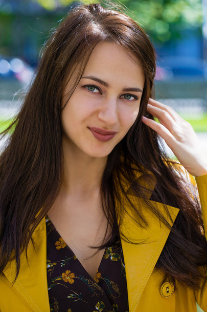 Close-up portrait of a young beautiful brunette in yellow jacket, spring outdoors street - Fotografie, Obrázek