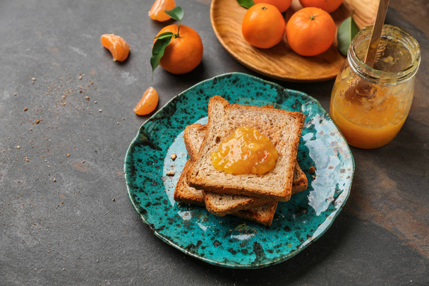 Placa con pan tostado y sabrosa mermelada de mandarina sobre mesa gris
 - Foto, imagen