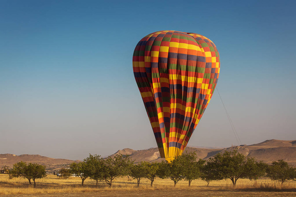 Landscape with colorful hot air balloon deflating over a beatiful blue sky in background - Foto, afbeelding