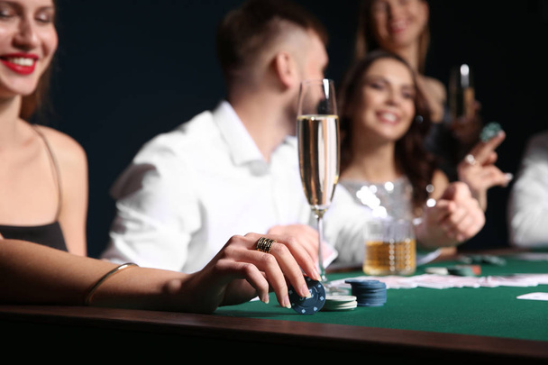 Женщина с бокалом шампанского сидит за столом с людьми, играющими в покер в казино
 - Фото, изображение