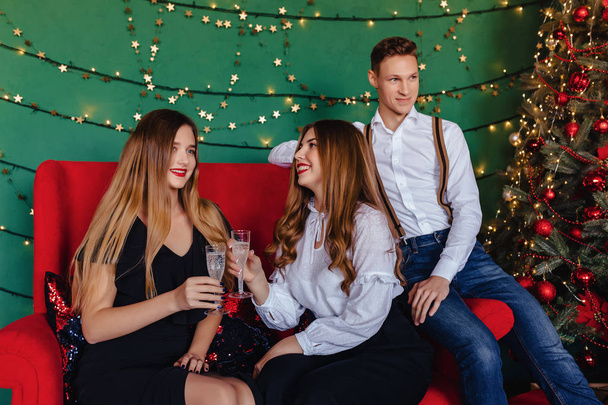 Молодая компания из двух девушек и один парень празднует новый год с бокалами шампанского дома
 - Фото, изображение