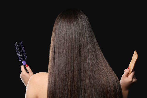 Mladá žena s krásné rovné vlasy hospodářství hřeben a kartáč na tmavém pozadí - Fotografie, Obrázek