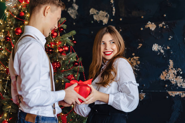 young attractive girl recieve present from man on the background of a Christmas tree, the theme of the new year - Fotó, kép
