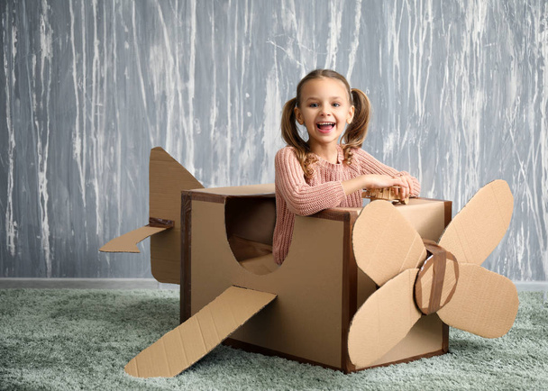 Little girl playing with cardboard airplane in room - Fotó, kép