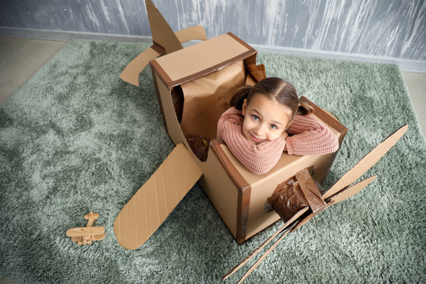 Little girl playing with cardboard airplane in room - Фото, изображение