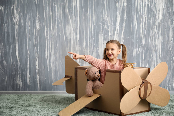 Маленька дівчинка грає з картонним літаком в кімнаті
 - Фото, зображення