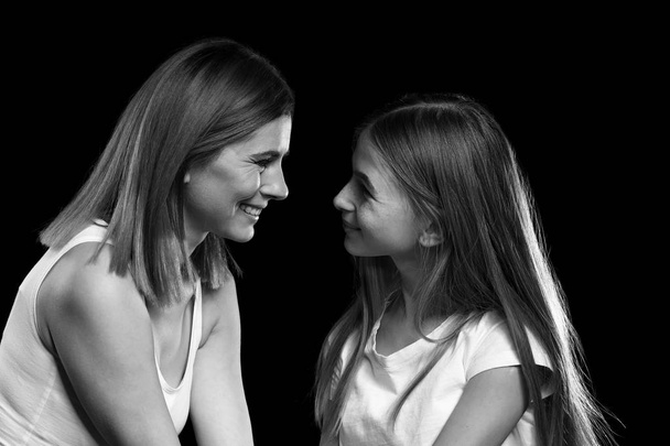 Black and white portrait of happy mother and daughter on dark background - 写真・画像