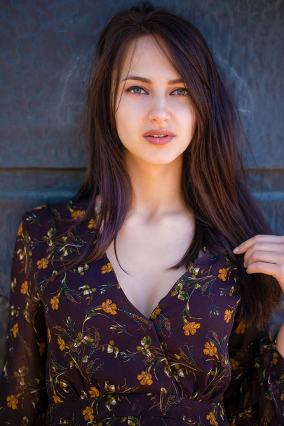 Beautiful young brunette woman in sexy brown dress, against still wall, summer outdoors - Fotografie, Obrázek
