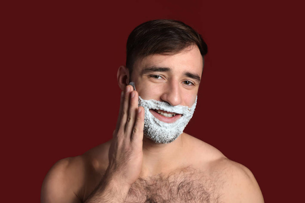 Handsome man with shaving foam on his face against color background - Foto, Bild