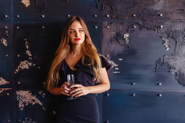 jovem menina atraente com uma taça de champanhe ou vinho no fundo escuro da parede
 - Foto, Imagem
