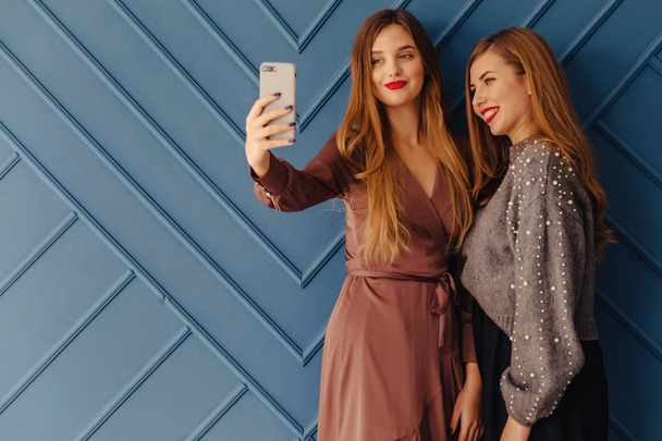 two attractive stylish young girls with smartphones on simple aqua background - Valokuva, kuva