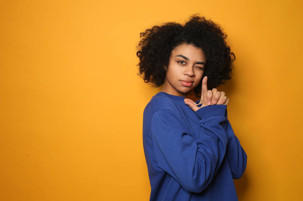 Portrait of young African-American woman showing "hand pistol" gesture on color background - Photo, Image