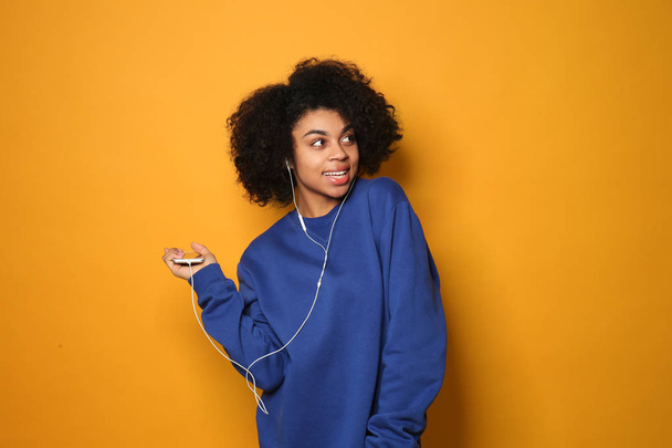 Portrait of young African-American woman listening to music on color background - Photo, Image