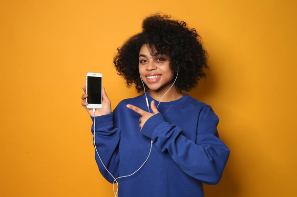 Portrait of young African-American woman listening to music on color background - Foto, afbeelding