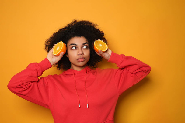 Portrait of young African-American woman with orange halves on color background - Photo, Image