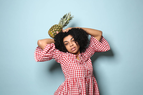 Portret van jonge Afro-Amerikaanse vrouw met ananas op kleur achtergrond - Foto, afbeelding
