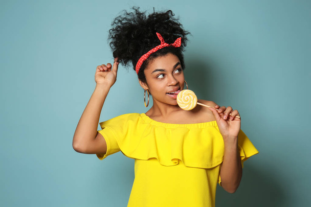 Portrait of young African-American woman with lollipop on color background - Photo, image